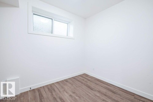 Bright room featuring wood-finish flooring, white walls, and a white-framed casement window with frosted glass - 5211 104A Street, Edmonton, AB 