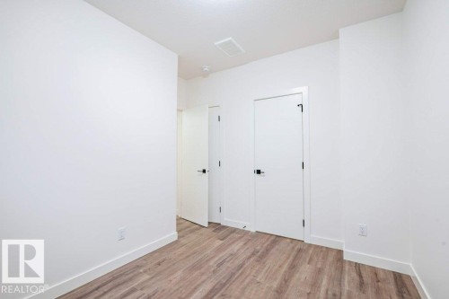 Interior space featuring wood-finish flooring, white walls, and modern white doors with black hardware - 5211 104A Street, Edmonton, AB 