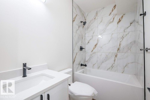 Bathroom featuring a white vanity with an integrated sink, matte black faucet, and a tiled shower-over-tub with matte black fixtures - 5211 104A Street, Edmonton, AB 
