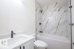 Bathroom featuring a white vanity with an integrated sink, matte black faucet, and a tiled shower-over-tub with matte black fixtures - 