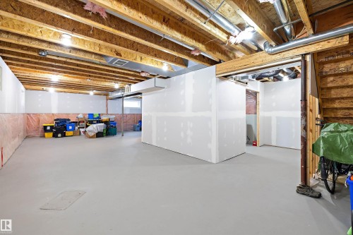 Unfinished basement with exposed wood ceiling joists and subfloor, featuring a concrete floor, partial drywall partitioning, and overhead utility lines - 3344 24 Avenue, Edmonton, AB 