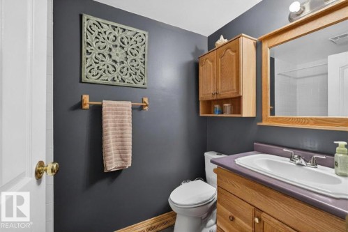 Bathroom featuring a wood-finish vanity with a built-in sink, a wood-framed mirror, and wood-finish cabinetry - 14648 54 Street, Edmonton, AB 