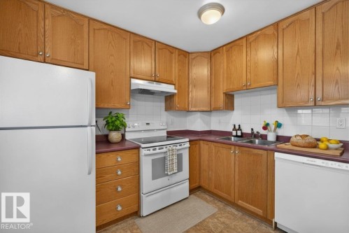 Kitchen featuring natural wood cabinetry, white appliances, dual basin sink, white tile backsplash, and durable flooring - 14648 54 Street, Edmonton, AB 