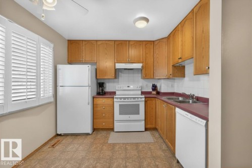 Kitchen featuring light wood cabinetry, white appliances, a double basin sink, white tile backsplash, and plantation shutters - 14648 54 Street, Edmonton, AB 