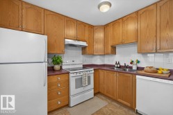 Kitchen featuring natural wood cabinetry, white appliances, dual basin sink, white tile backsplash, and durable flooring - 