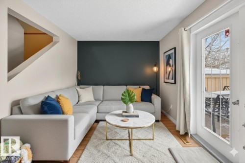 Living area featuring light wood-finish flooring, a contemporary dark accent wall, and a staircase with a unique angular cutout - 14648 54 Street, Edmonton, AB 