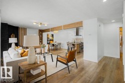Open-concept living area featuring wood-finish flooring, a contemporary ceiling light fixture, a black accent wall, and a built-in shelving unit - 