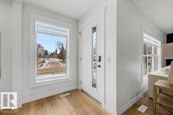 Entryway featuring wood-finish flooring, a white front door with full-length glass inserts, and a large picture window with layered window treatments - 