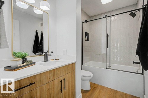Bathroom featuring a wood-finish vanity with quartz countertop and undermount sink, a gold-framed rectangular mirror, and a tub with a sliding glass enclosure and tiled surround - 49 Galloway Drive, Sherwood Park, AB - Indoor Photo Showing Bathroom