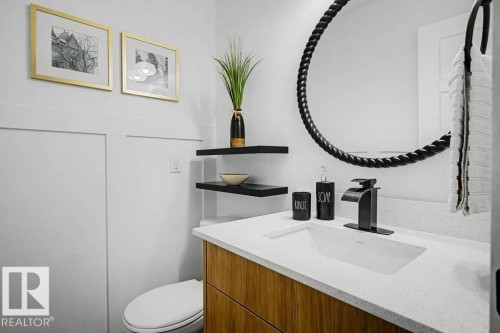 Bathroom featuring a wood-finish vanity with a white countertop and integrated sink, matte black faucet, and a large round mirror with a textured frame - 49 Galloway Drive, Sherwood Park, AB - Indoor Photo Showing Bathroom