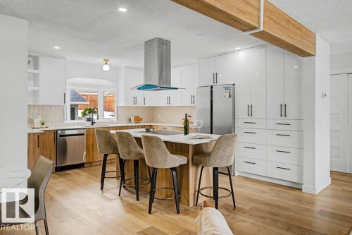 Contemporary kitchen featuring a central island with countertop seating, high-gloss white cabinetry, integrated stainless steel appliances, wood-finish flooring, and a decorative exposed wood beam - 49 Galloway Drive, Sherwood Park, AB - Indoor