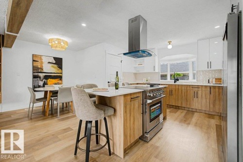 Expansive kitchen featuring a center island with integrated range, stainless steel vent hood, wood-finish flooring, and two-tone cabinetry with white upper and wood-finish lower units - 49 Galloway Drive, Sherwood Park, AB - Indoor Photo Showing Kitchen