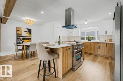 Expansive kitchen featuring a center island with integrated range, stainless steel vent hood, wood-finish flooring, and two-tone cabinetry with white upper and wood-finish lower units - 