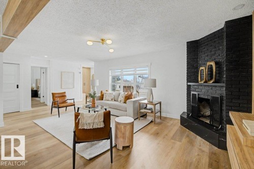Living area featuring light wood-finish flooring, a contemporary ceiling light fixture, and a prominent black brick fireplace with a marble hearth - 49 Galloway Drive, Sherwood Park, AB - Indoor Photo Showing Living Room With Fireplace