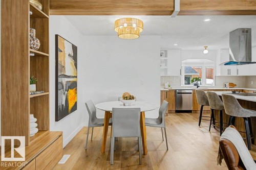 Open-concept living area featuring wood-finish flooring, a contemporary chandelier, built-in shelving, a kitchen island with seating, and stainless steel appliances - 49 Galloway Drive, Sherwood Park, AB - Indoor Photo Showing Dining Room