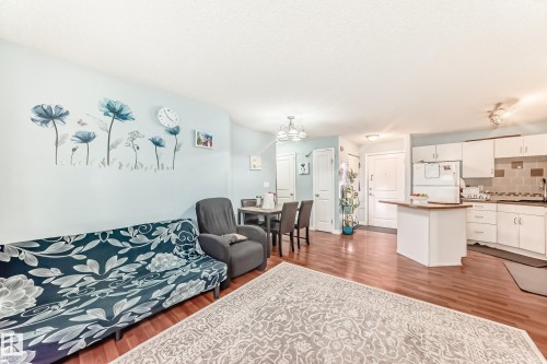 Open-concept living area featuring wood-finish flooring, a dining space with a chandelier, and a kitchen with white cabinetry and a breakfast bar - 108 10535 122 Street, Edmonton, AB 