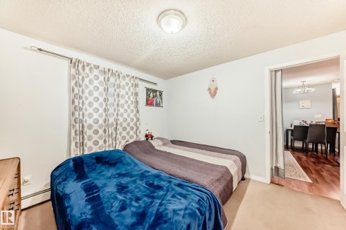 Carpeted room featuring a ceiling-mounted light fixture, light-colored walls, and a window with patterned drapes - 108 10535 122 Street, Edmonton, AB 