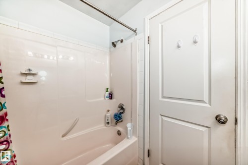 Bathroom featuring a tub/shower combination with a built-in ledge, white tile surround, and a brushed nickel shower head - 108 10535 122 Street, Edmonton, AB 