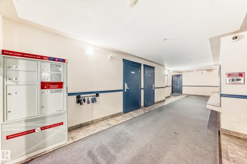 Common area hallway with carpet flooring and wall-mounted parcel lockers - 108 10535 122 Street, Edmonton, AB 