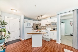 Kitchen featuring white cabinetry, white appliances, a light wood-finish countertop, a central island, and wood-finish flooring - 