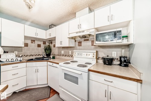 Kitchen featuring white cabinetry, light-toned countertops, a white electric range, and a built-in dishwasher - 108 10535 122 Street, Edmonton, AB 