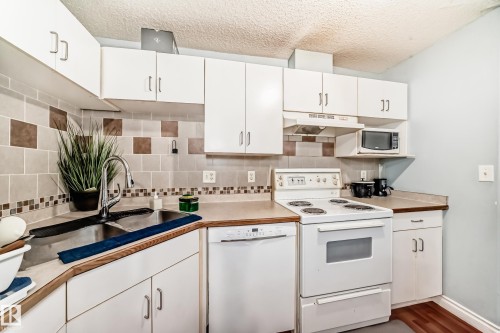 Kitchen featuring white cabinetry, wood-finish countertops, stainless steel sink, and a patterned tile backsplash - 108 10535 122 Street, Edmonton, AB 