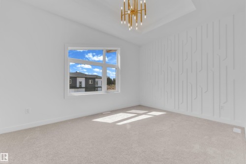 Spacious room featuring a large window, decorative accent wall, tray ceiling, and a modern gold chandelier - 177 Graybriar Drive, Stony Plain, AB 