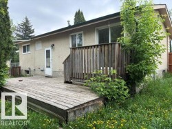 Rear facade featuring a wooden deck with railing, stucco exterior, and multiple windows - 