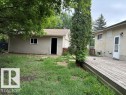 Spacious backyard featuring a detached garage with vinyl siding, a wooden deck, and a mature tree - 5316 107 Street, Edmonton, AB 