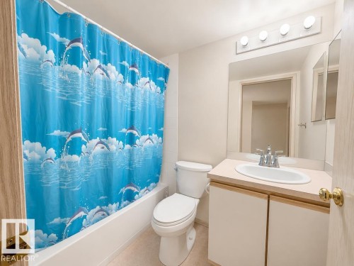 Bathroom featuring a built-in bathtub with white tile surround, a single vanity with a white countertop and integrated sink, and a toilet - 218 5065 31 Avenue, Edmonton, AB 