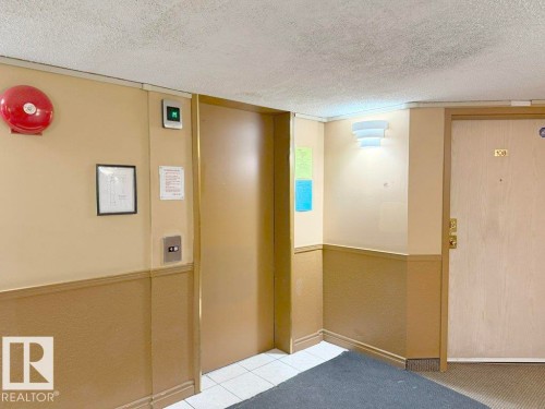 Interior hallway featuring an elevator entrance with call buttons and a contemporary wall sconce - 218 5065 31 Avenue, Edmonton, AB 