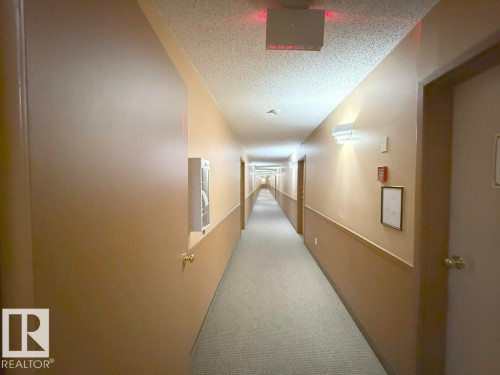 Hallway featuring carpet flooring, neutral-toned walls with wainscoting, wall-mounted light fixtures, and multiple entry doors - 218 5065 31 Avenue, Edmonton, AB 