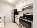 Kitchen featuring stainless steel appliances, white cabinetry with wood-finish trim, a light-toned countertop, white tile backsplash, and a double basin sink - 218 5065 31 Avenue, Edmonton, AB 