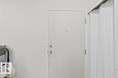 White interior door with brass hardware and a peephole, framed by white trim - 218 5065 31 Avenue, Edmonton, AB 