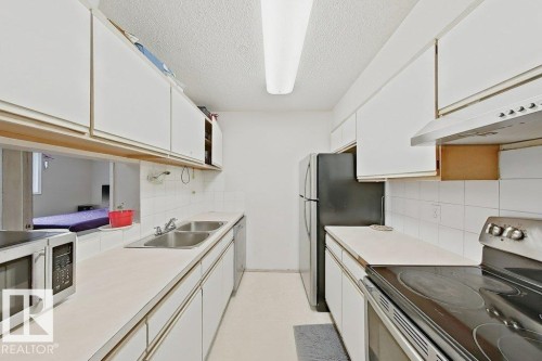 Galley kitchen featuring white cabinetry, dual basin stainless steel sink, black refrigerator, and a stainless steel oven range with an overhead vent - 218 5065 31 Avenue, Edmonton, AB 