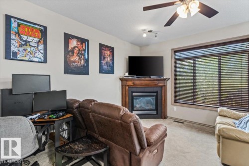 Recessed fireplace with wood-finish mantel and hearth, large window with horizontal blinds, overhead ceiling fan with light fixture, and neutral wall paint - 229 41 Summerwood Boulevard, Sherwood Park, AB - Indoor With Fireplace