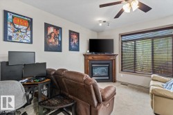 Recessed fireplace with wood-finish mantel and hearth, large window with horizontal blinds, overhead ceiling fan with light fixture, and neutral wall paint - 