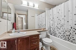 Full bathroom featuring a single vanity with wood-finish cabinetry, a neutral countertop, an integrated sink, and a large wall-mounted mirror - 