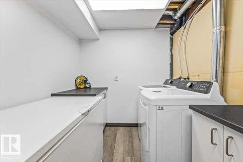 Dedicated laundry area featuring a washer and dryer, wood-finish flooring, and ample counter space with dark countertops - 229 41 Summerwood Boulevard, Sherwood Park, AB - Indoor Photo Showing Laundry Room