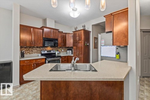 Kitchen featuring wood-finish cabinetry, stainless steel appliances, a mosaic tile backsplash, and a double basin sink with a chrome faucet - 229 41 Summerwood Boulevard, Sherwood Park, AB - Indoor Photo Showing Kitchen With Double Sink