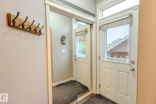 Entryway featuring a white paneled door with integrated window and transom, wood-finish coat rack, and full-length mirrored closet doors - 7207 14A Avenue, Edmonton, AB - Indoor Photo Showing Other Room