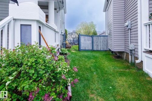 Side yard featuring a green lawn, established landscaping, white porch railings, and a decorative wrought iron gate with wood fencing - 7207 14A Avenue, Edmonton, AB - Outdoor