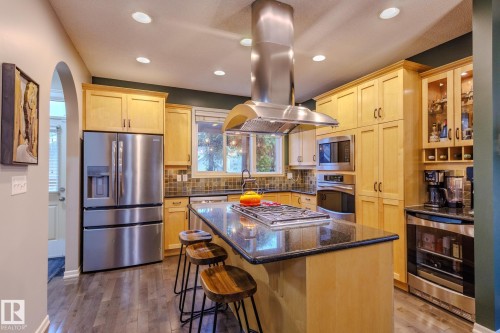Kitchen featuring an expansive center island with a gas cooktop, a stainless steel range hood, ample light wood cabinetry, recessed lighting, and wood-finish flooring - 7207 14A Avenue, Edmonton, AB - Indoor Photo Showing Kitchen