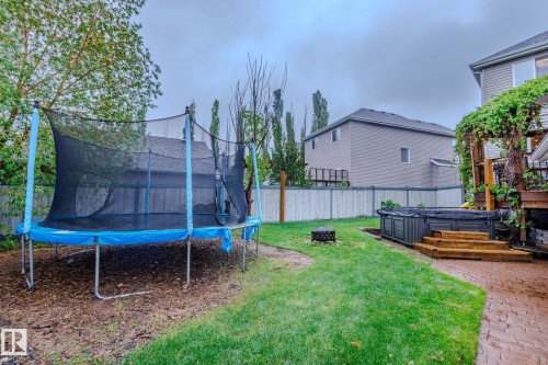 Expansive backyard featuring a hot tub with wood stairs, a decorative pergola with climbing greenery, a paved patio area, and a green lawn with a fire pit - 7207 14A Avenue, Edmonton, AB - Outdoor With Exterior
