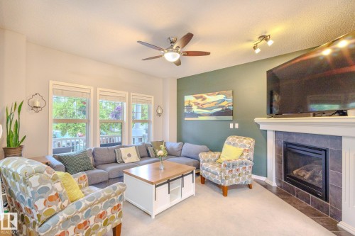 Living area featuring a tiled fireplace with white mantel, a ceiling fan with integrated lighting, and multiple windows with white trim - 7207 14A Avenue, Edmonton, AB - Indoor Photo Showing Living Room With Fireplace