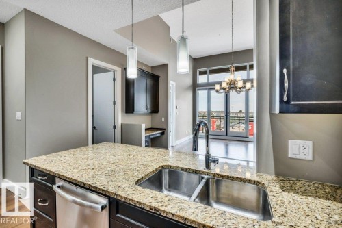 Kitchen island featuring a double basin stainless steel sink, gooseneck faucet, and integrated dishwasher - 607 11080 Ellerslie Road, Edmonton, AB - Indoor Photo Showing Kitchen With Double Sink