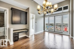 Spacious room featuring wood-finish flooring, a built-in desk with dark cabinetry and a stone-finish countertop, a multi-light chandelier, and expansive sliding glass doors with transom windows - 