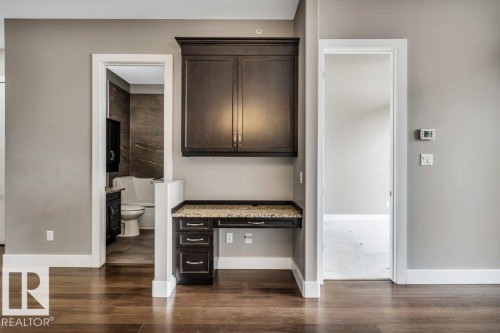 Built-in desk area featuring dark wood-finish cabinetry, a stone-finish countertop, and integrated drawers - 607 11080 Ellerslie Road, Edmonton, AB - Indoor Photo Showing Other Room