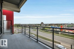 Concrete balcony with black metal and clear glass railings, a frosted glass privacy panel, and exterior red architectural accents - 
