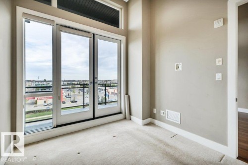 Light-filled room featuring a broad window and glass French door leading to a balcony with black metal railings - 607 11080 Ellerslie Road, Edmonton, AB - Indoor Photo Showing Other Room